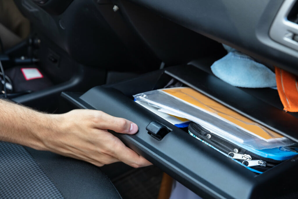 A person opens the glove box of their car which contains registration and other documents.