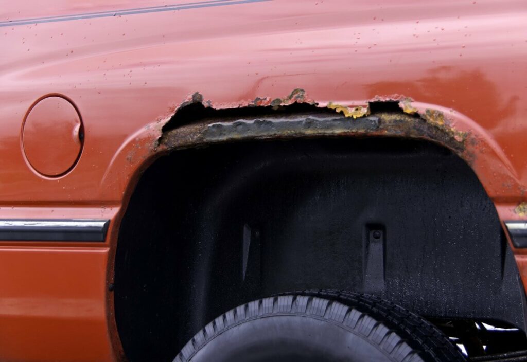 A closeup of a red truck’s wheel well and the rust that is accumulating along it