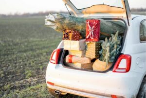 A white hatchback’s trunk is full of wrapped gifts, a Christmas tree, and holiday decorations.