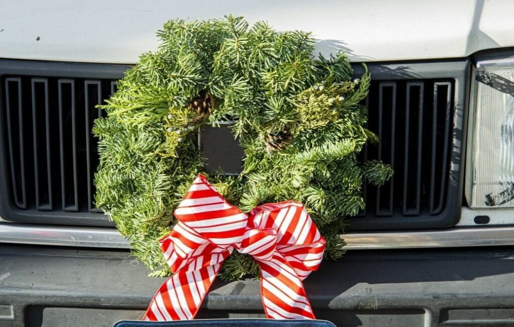 The front grill of a large van decorated with a green wreath adorned with a red and white bow.