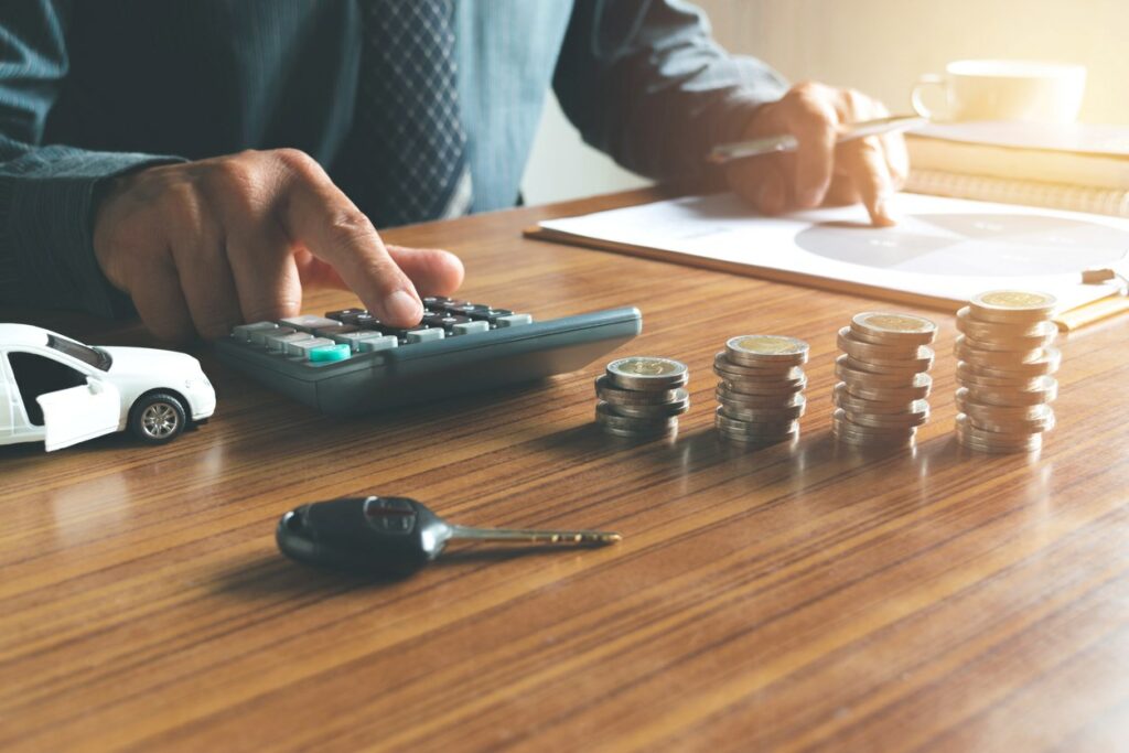 A man uses a calculator and a bar graph to calculate savings for a car with coins, keys, and a toy car on the desk.