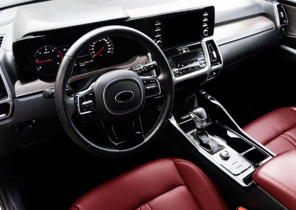 The interior of a modern car includes a steering wheel, dashboard, red leather seats, and a gear stick.