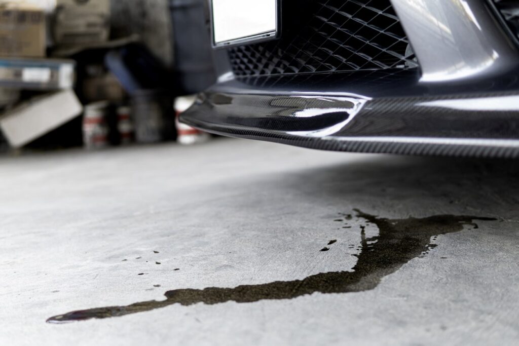 The cement floor under a car is stained and wet with leaking fluid.