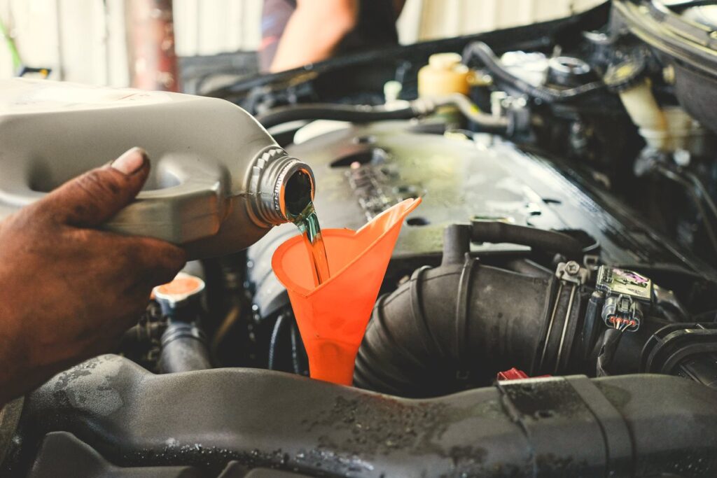 An automotive technician uses a funnel to top off transmission fluid.