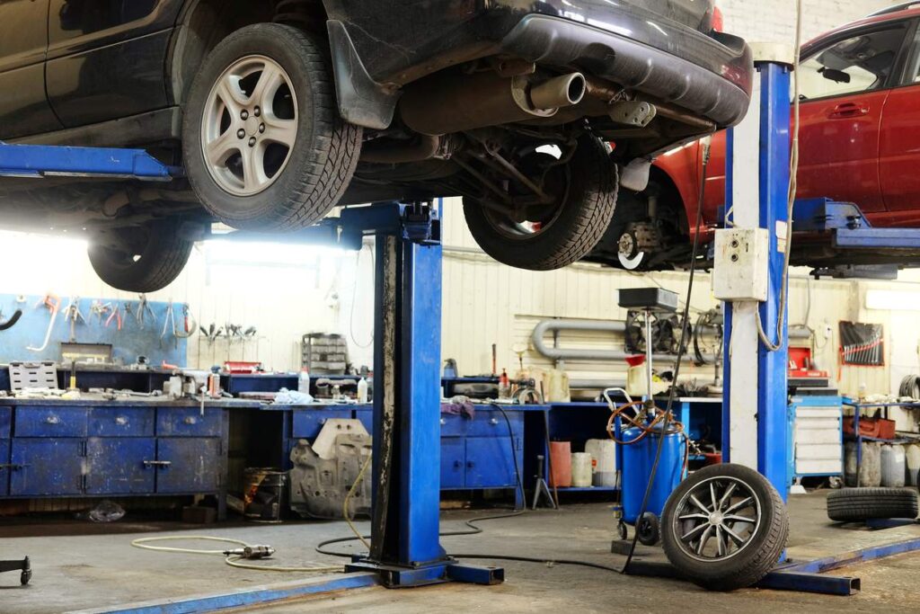 The interior of an auto mechanic shop with two cars elevated for repairs and various tools along the back wall.