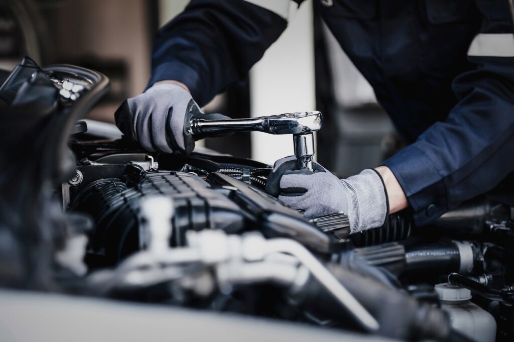 A professional mechanic in gray gloves repairs the internal components of a vehicle.