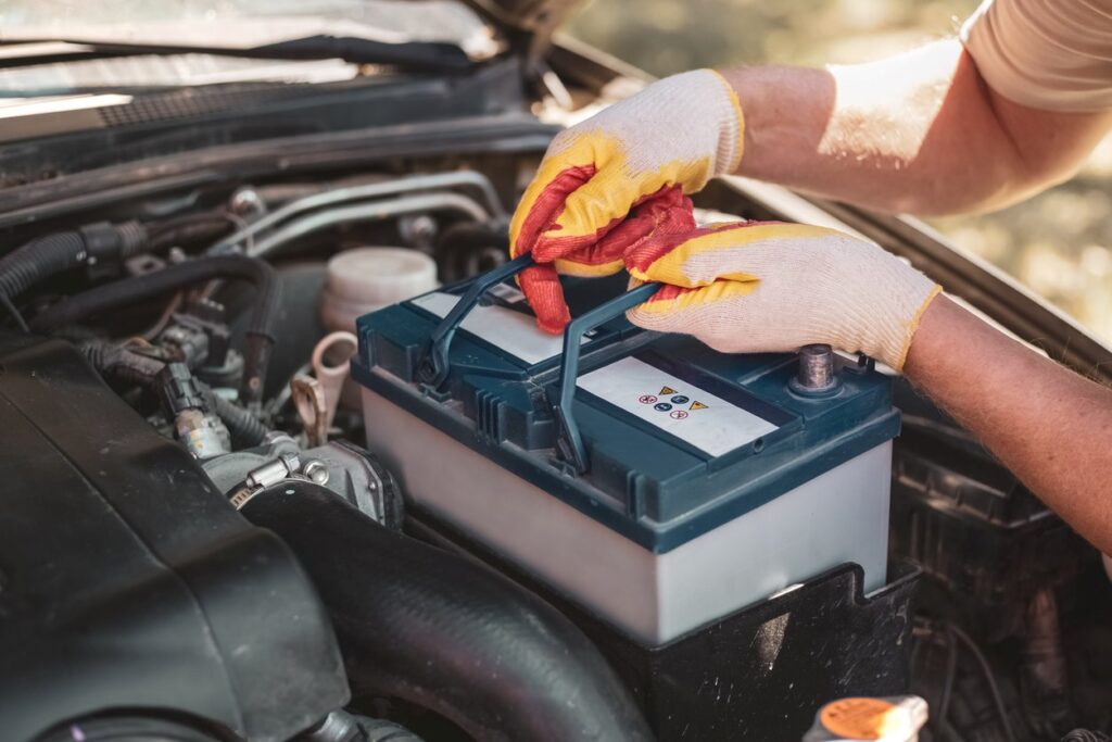 A person wearing gloves carefully changes their car battery. 