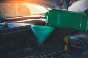 Synthetic motor oil is being poured into the engine via a green funnel.