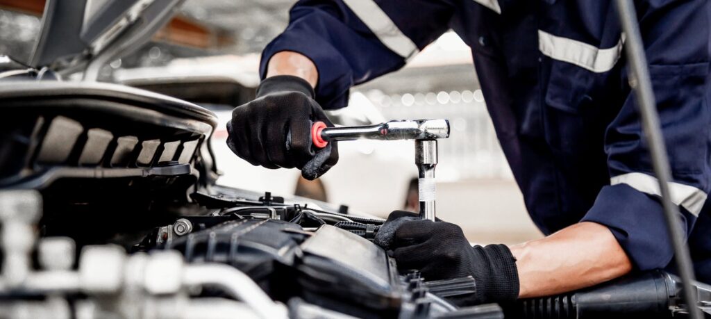 A mechanic uses a socket wrench to loosen a bolt in the engine bay of a car.