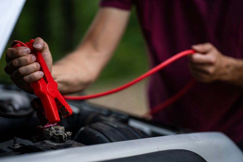 A person carefully applies a red cable to the contact posts on a car battery during a jump-start.