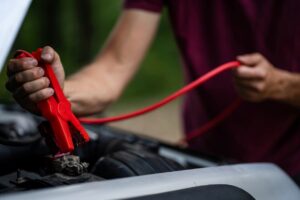 A person carefully applies a red cable to the contact posts on a car battery during a jump-start.