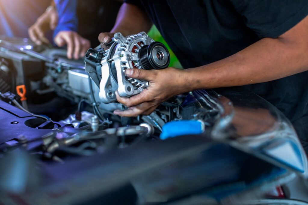An alternator being removed from a car’s engine bay during an in-shop repair.