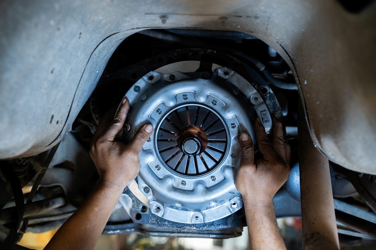 A new clutch plate is installed by a mechanic on a manual transmission of a lifted vehicle.