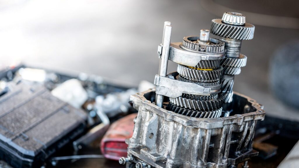 A transmission gearbox sits open for maintenance on a mechanic’s workbench.