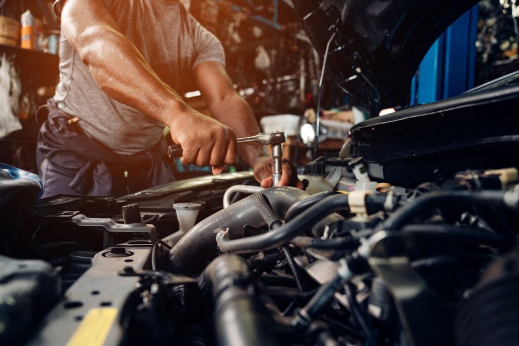 An auto repair mechanic works on an engine in a car repair service station.