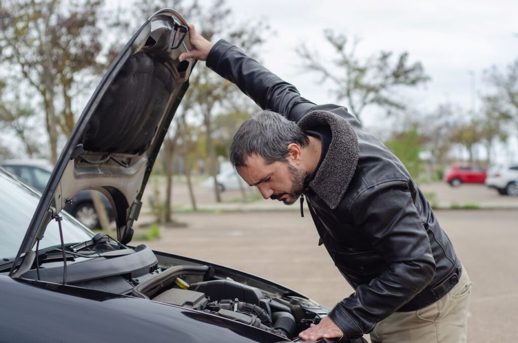 A man checking his car engine with the hood open.