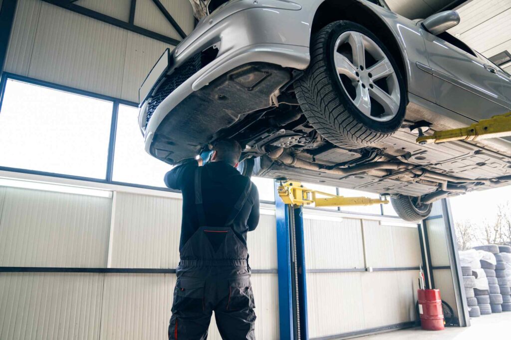 Mechanic inspecting the undercarriage of a car on a lift during a spring service appointment.