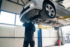Mechanic inspecting the undercarriage of a car on a lift during a spring service appointment.