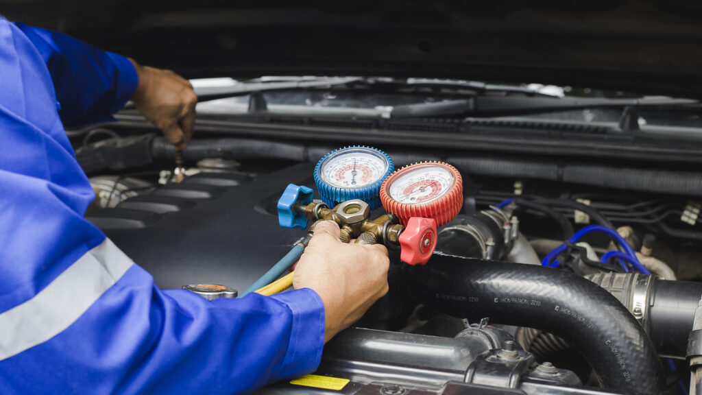 Technician checking refrigerant gauges while servicing a vehicle air conditioning system under the hood.
