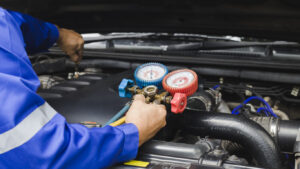 Technician checking refrigerant gauges while servicing a vehicle air conditioning system under the hood.