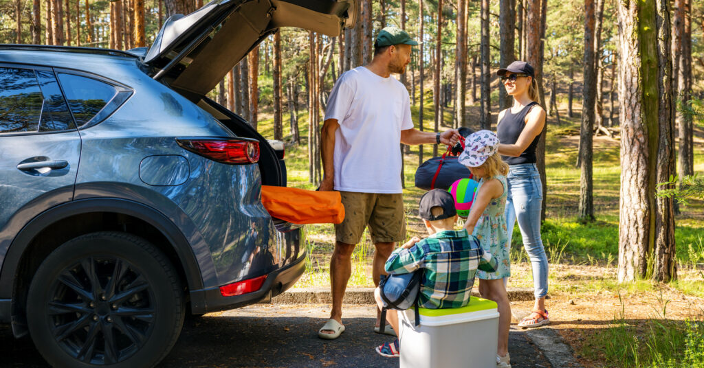 Family preparing to leave for a long summer road trip beside a packed SUV.