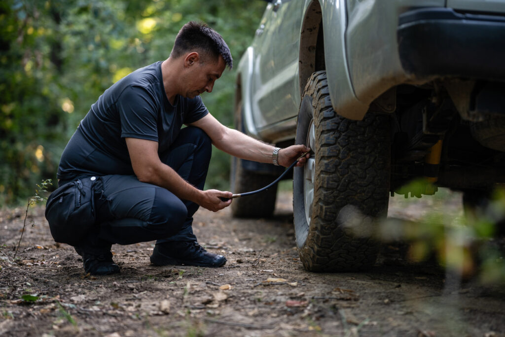 Driver checking tire pressure on an SUV before a long summer road trip.