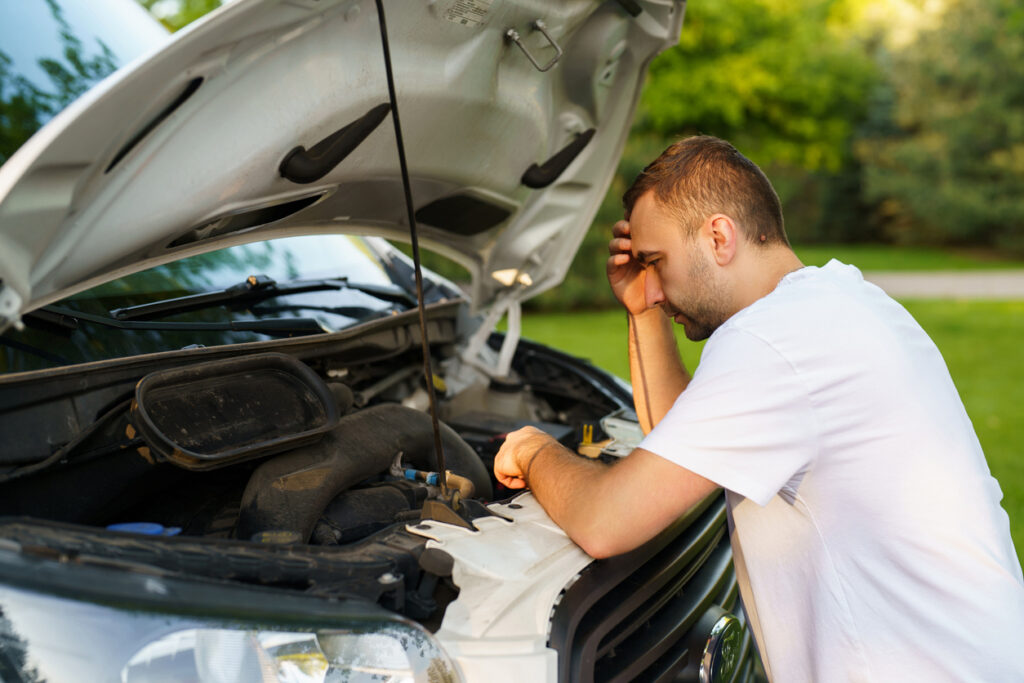 Driver inspecting the engine compartment of a vehicle with the hood open.