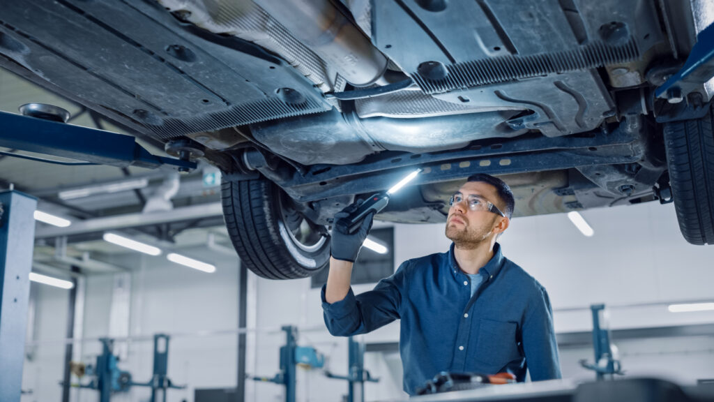 A mechanic inspecting the underside of a vehicle with a flashlight while it is raised on a lift.