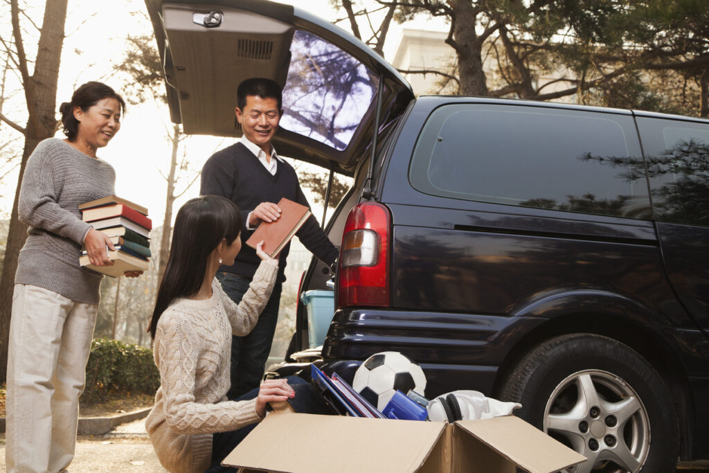Two parents and a young woman loading books and belongings into a minivan.