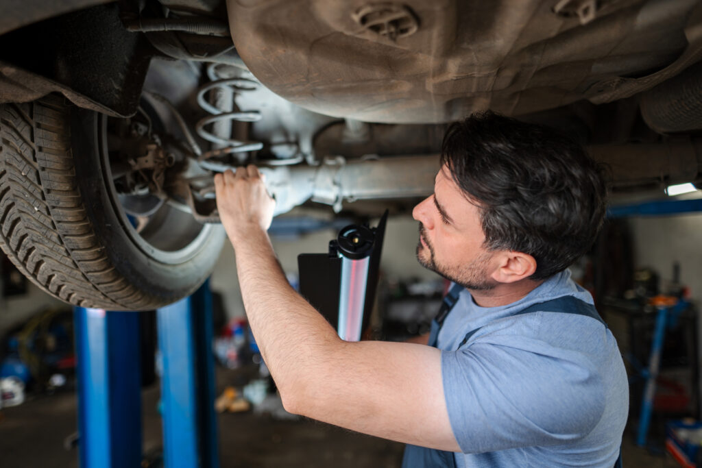 A mechanic inspecting a vehicle’s rear suspension and coil spring on a lift.